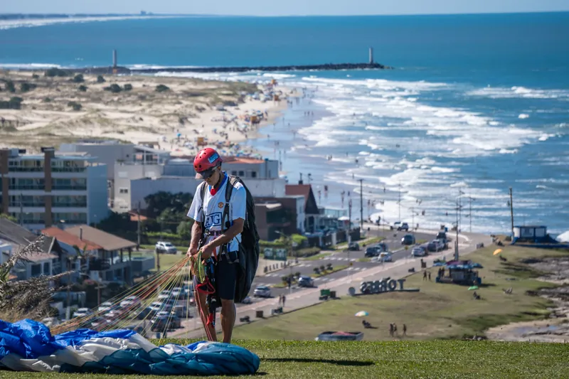 Piloto de parapente prepara o equipamento no Morro da Guarita, com a Praia Grande e o letreiro de Torres (RS) ao fundo