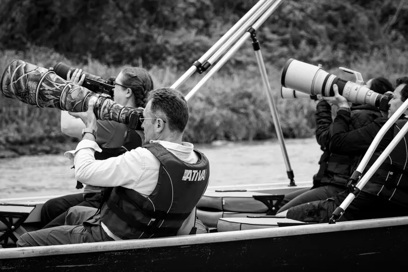 Fotógrafos com teleobjetivas apontadas para a margem do rio, a bordo de um barco de observação no Pantanal