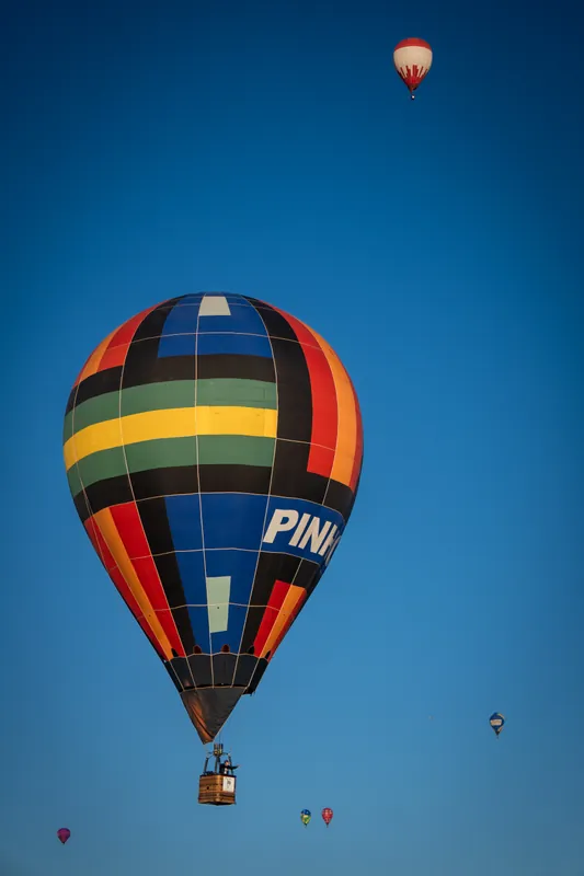Diversos balões coloridos voando lado a lado em céu azul durante festival de balonismo